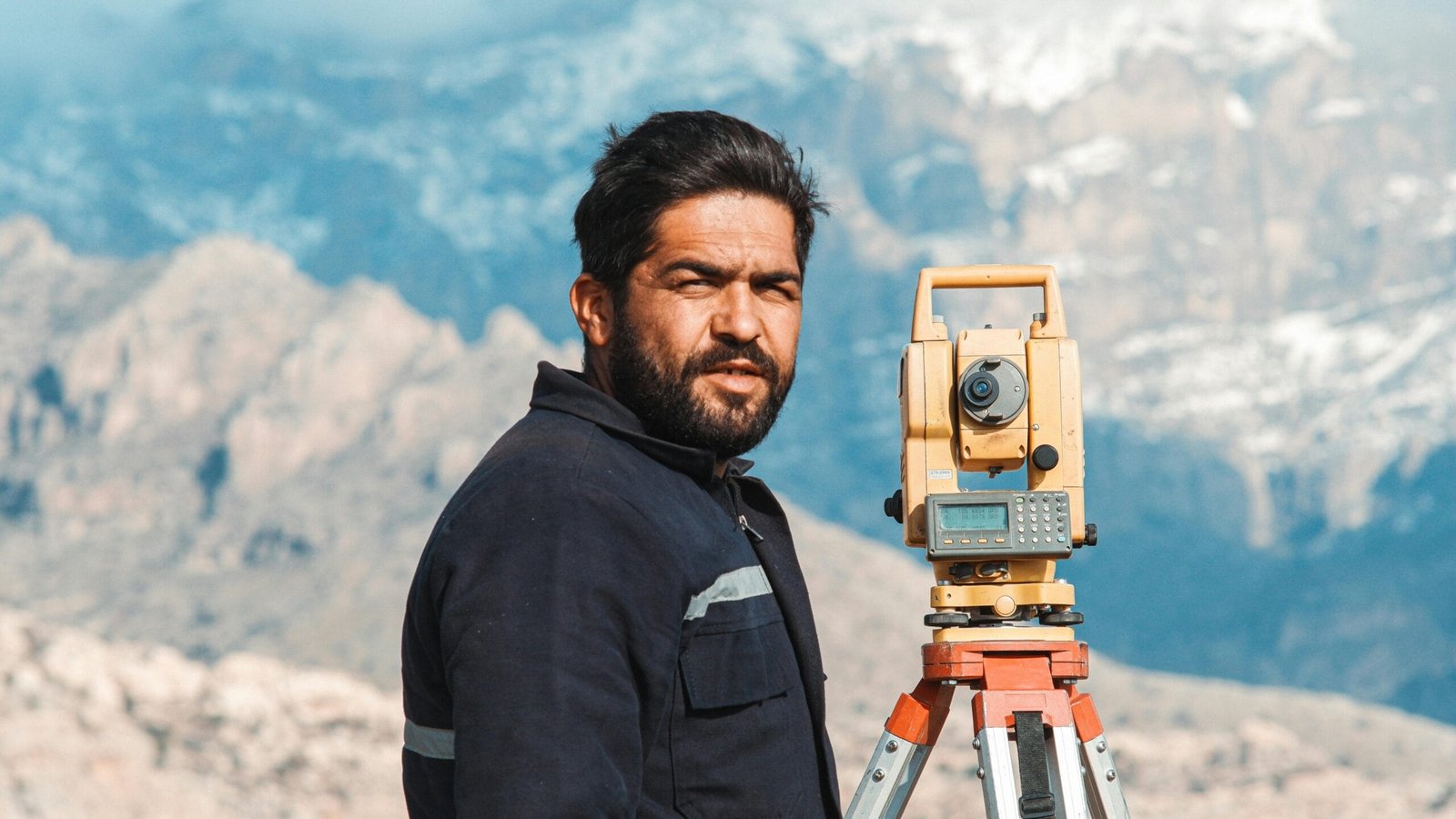 A surveyor outdoors with equipment against a scenic mountain backdrop.