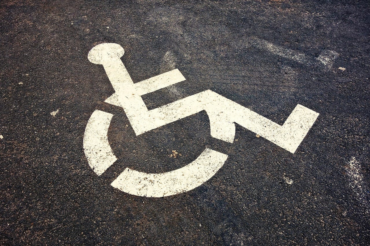 White wheelchair accessibility symbol painted on weathered asphalt in a parking area.